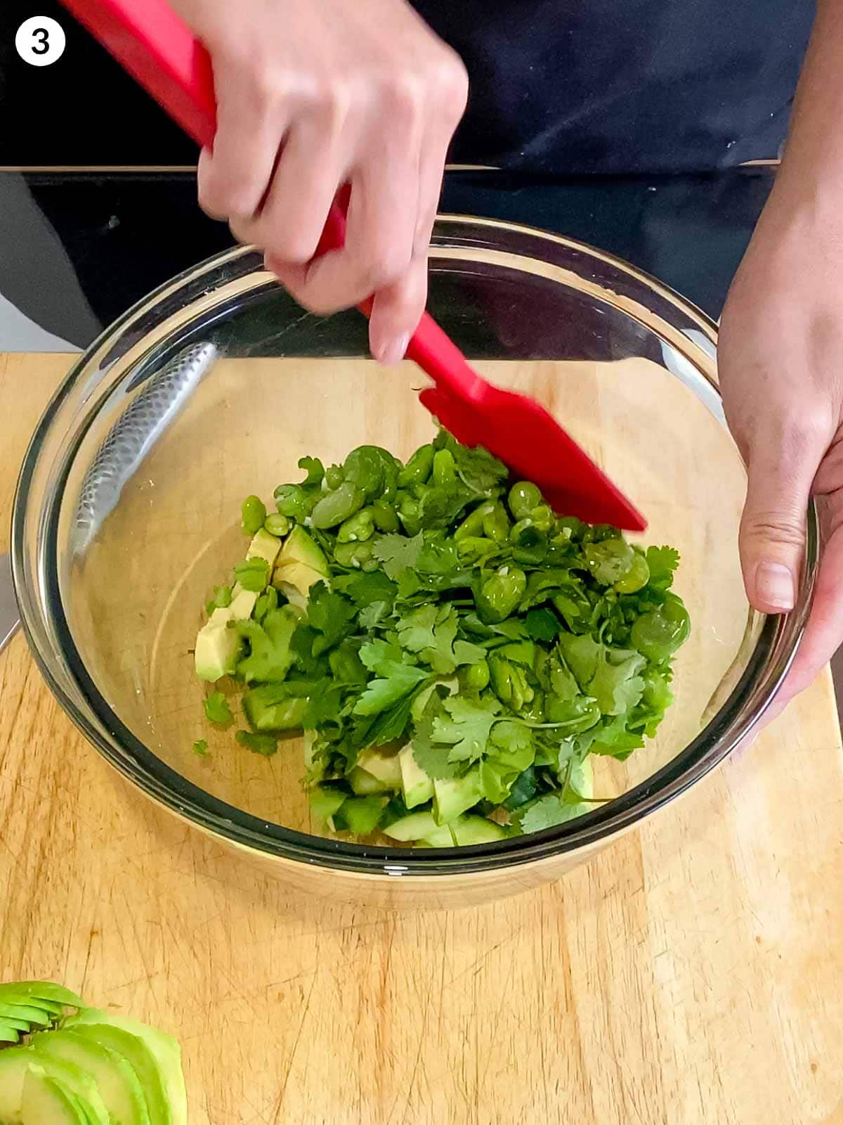Person mixing ingredients for Creamy Cucumber Avocado Saladin a mixing bowl