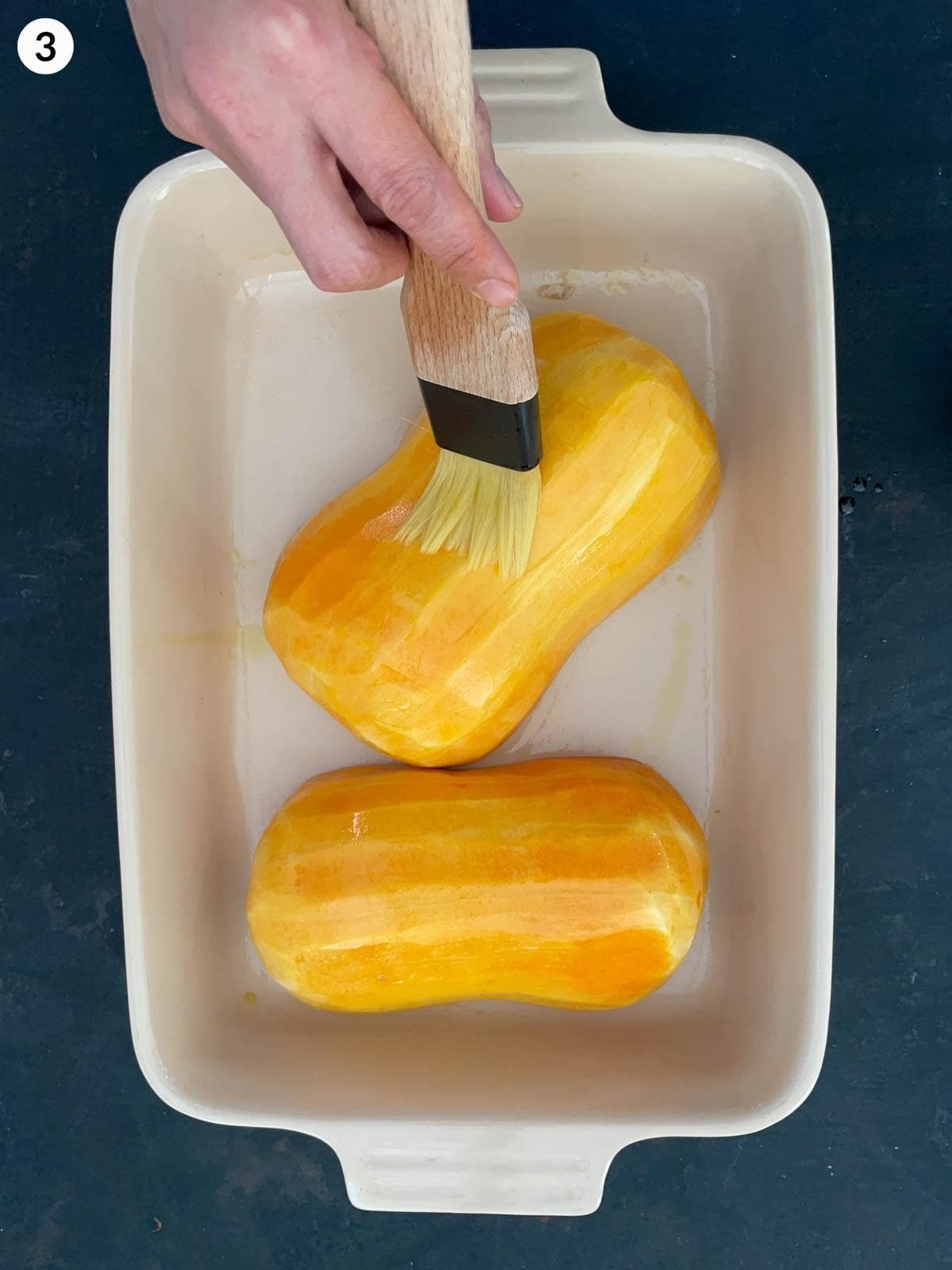 Basting butternut squash halves with olive oil in a baking dish