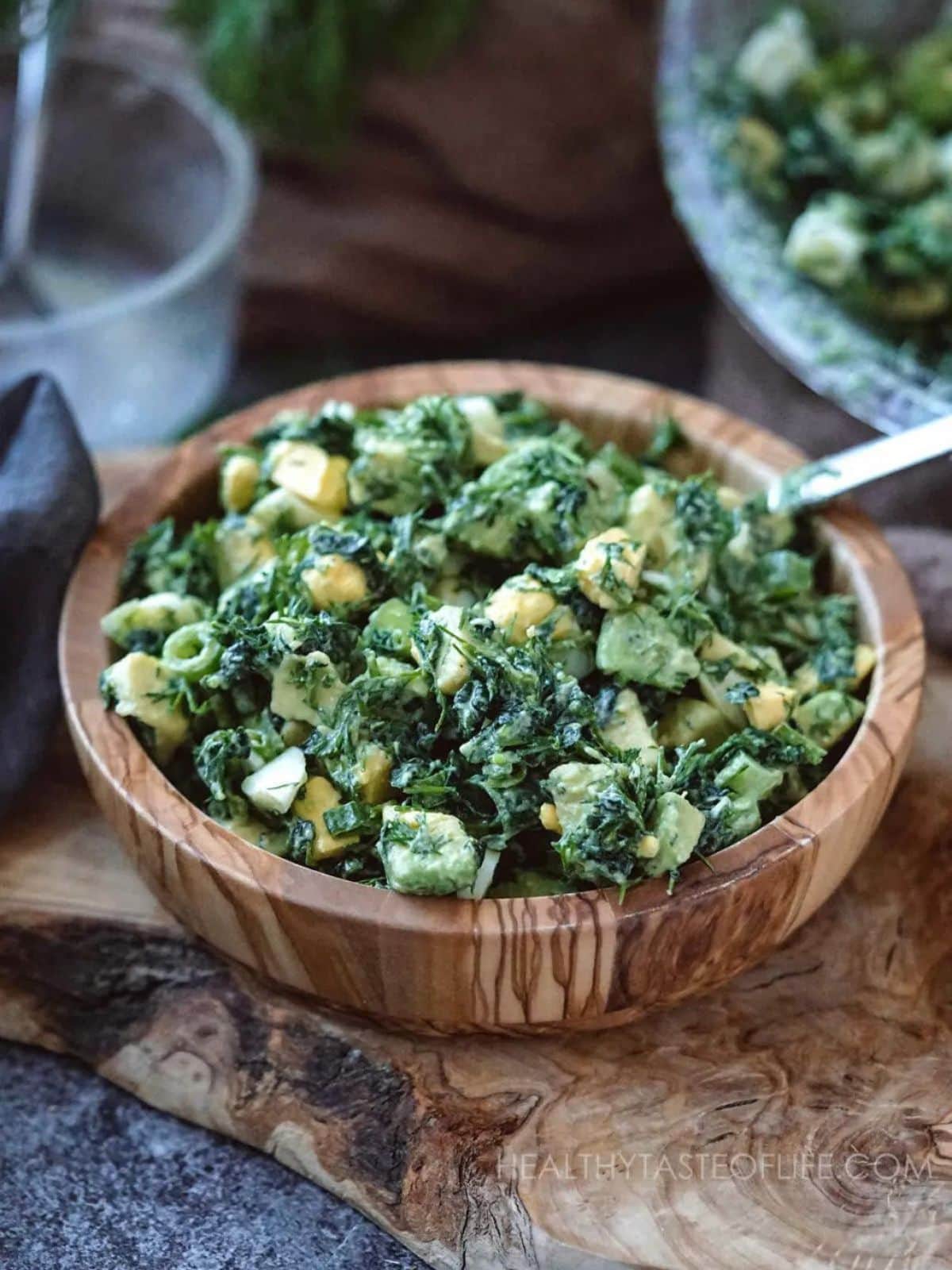Avocado kale salad with egg in a wooden salad bowl and a spoon