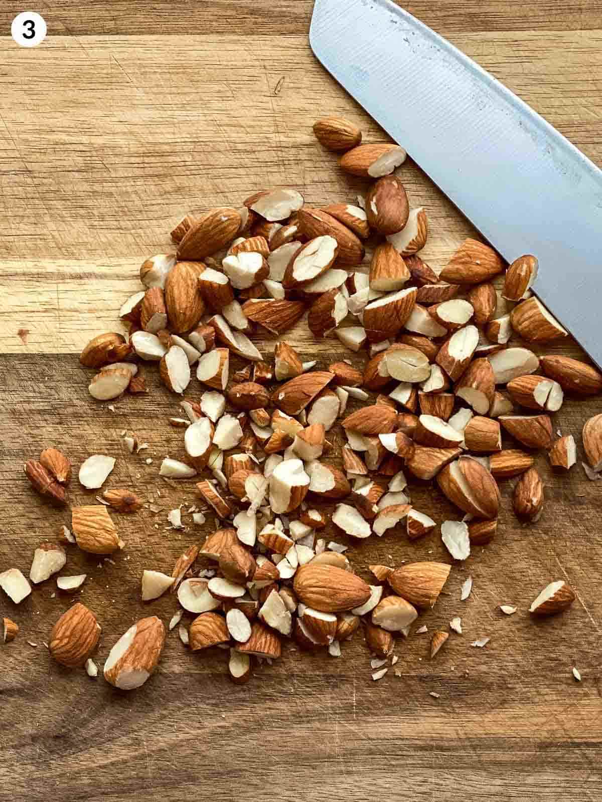 chopped almonds with a knifeon the side on a wooden chopping board