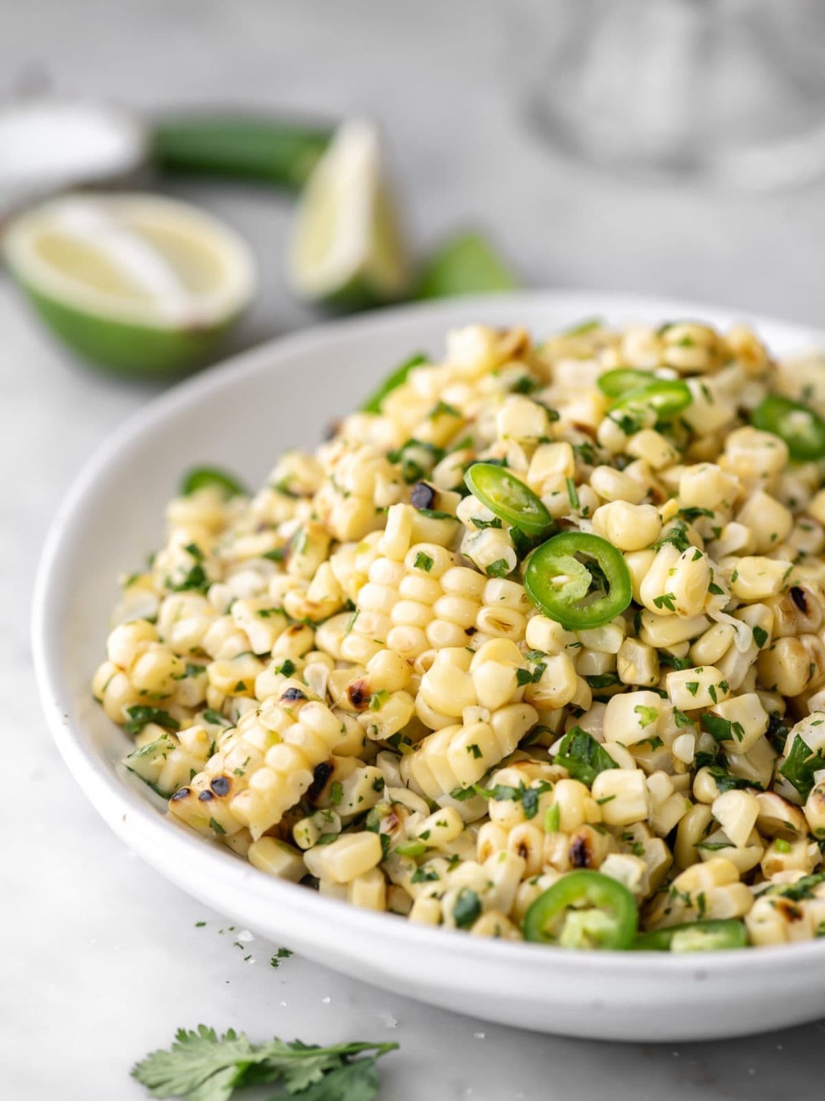 Corn salad with serrano peppers in a white bowl and lime in the background