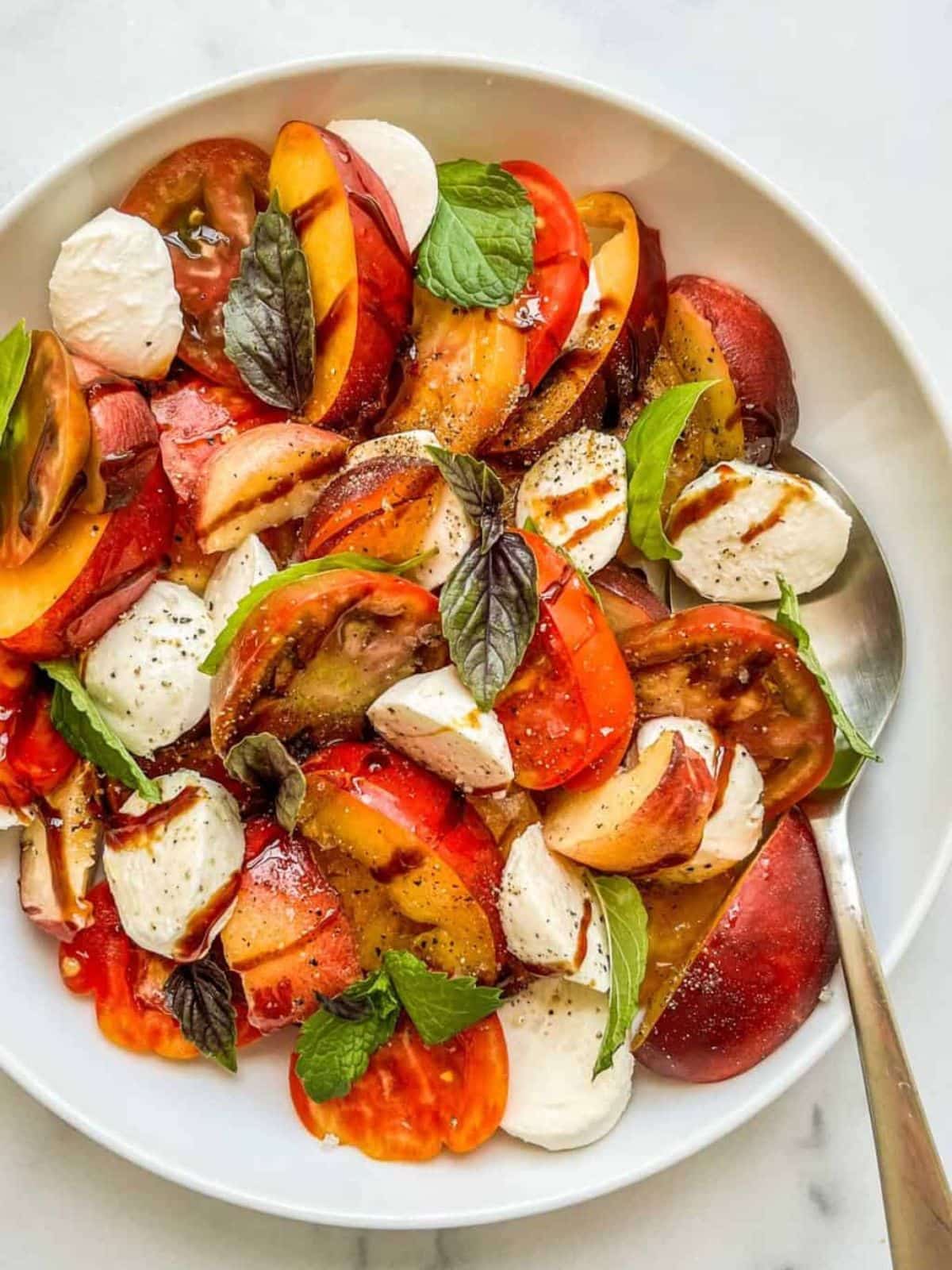 Heirloom tomato salad in a white bowl with a spoon