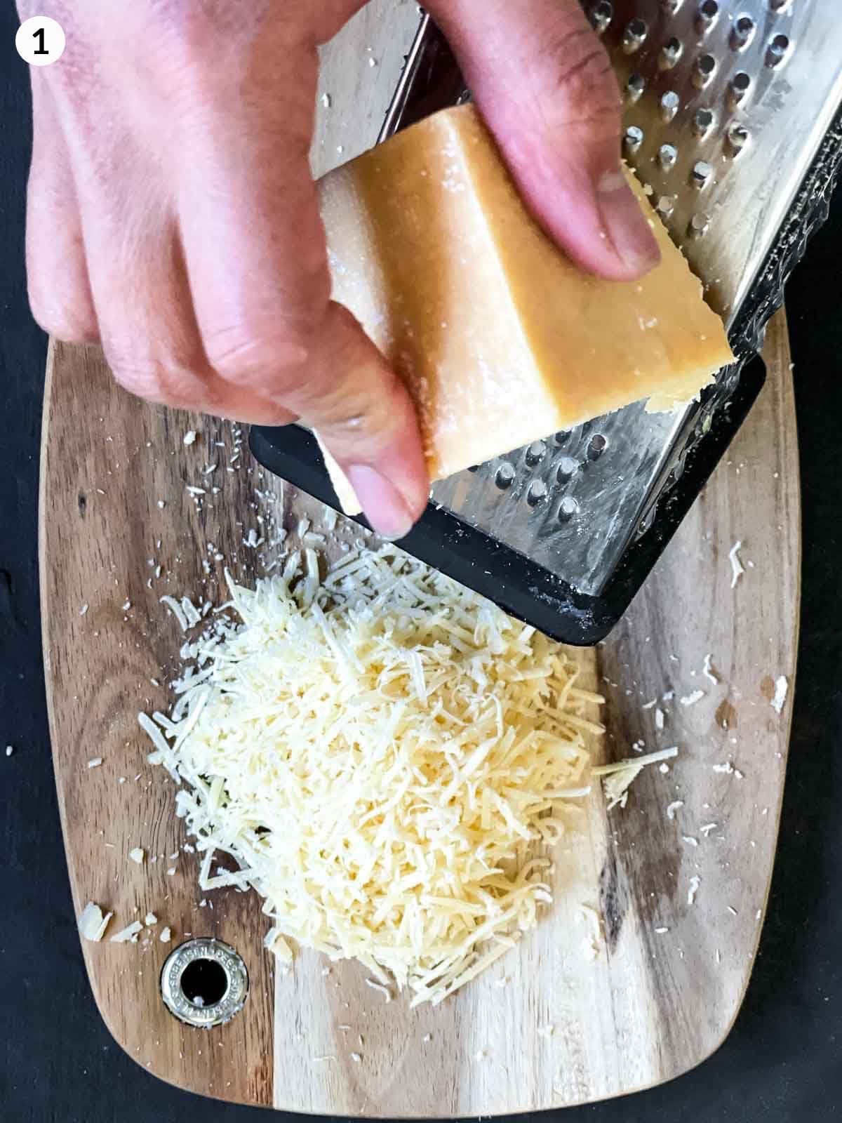 Hand grating parmesan cheese block with a grater on a wooden block