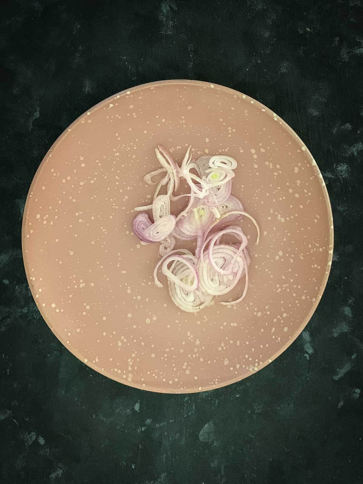 Sliced shallots on a white and pink speckled plate