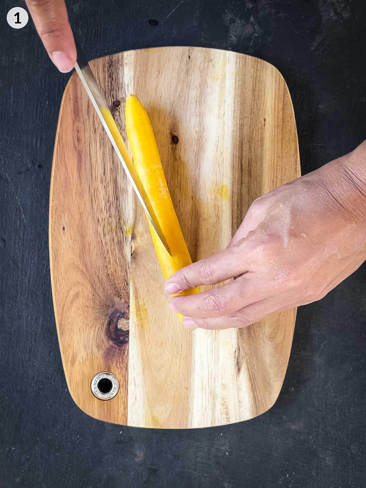 Cutting yellow carrot lengthwise with a knife on a chopping board