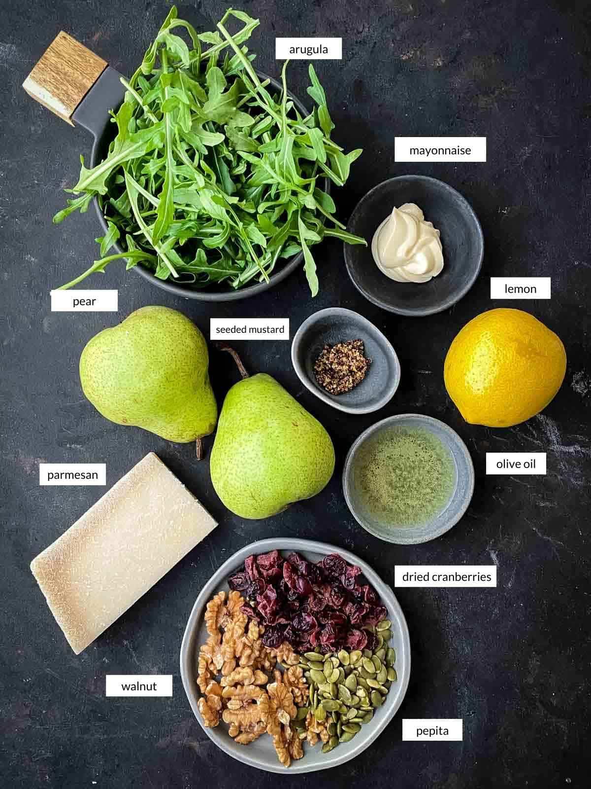 pear salad ingredients with arugula, pear, parmesan, walnuts, pepita, dried cranberries, mayo, oil, lemon and seeded mustard.