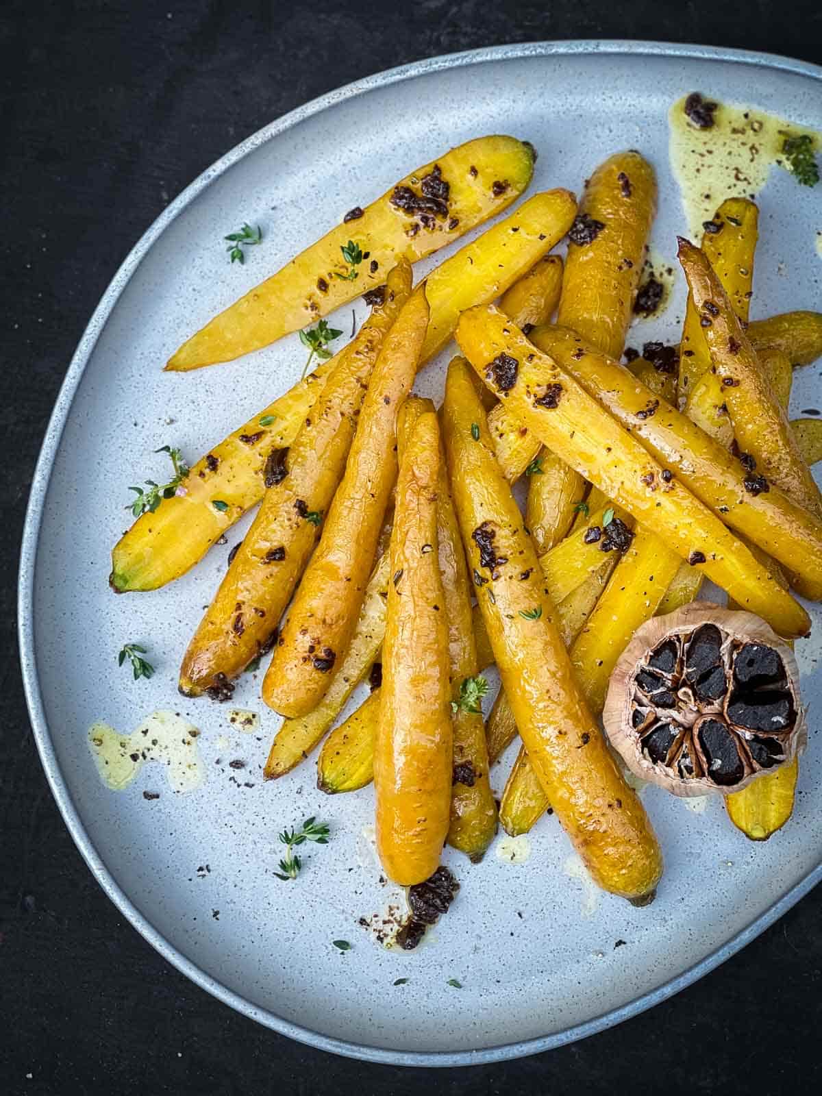 Roasted yellow carrots and black garlic on a blue salad platter