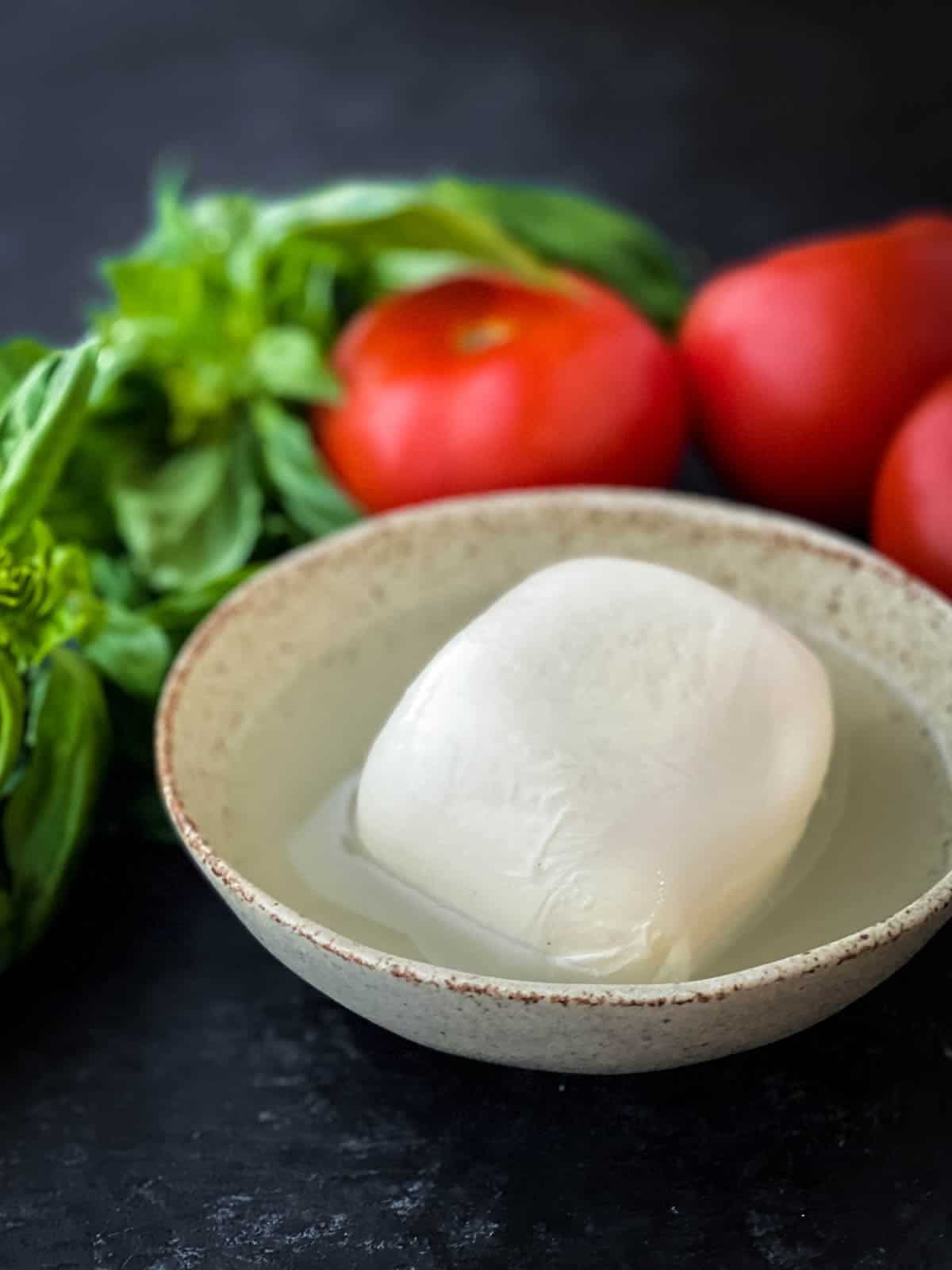 Buffalo mozzarella in brine in a bowl with basil and tomato in the background