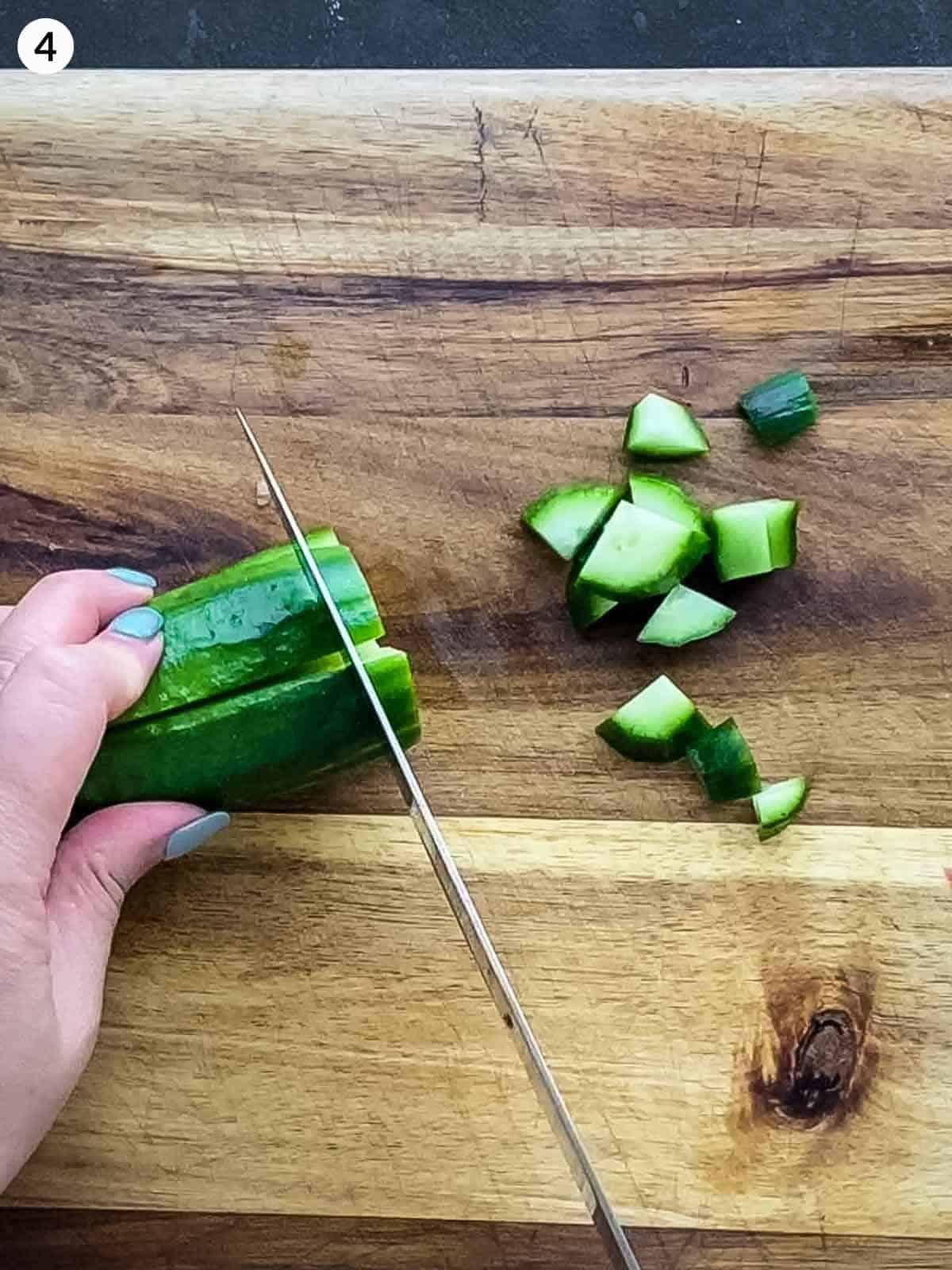 hands using knife to cut cucumber pieces on wooden chopping board
