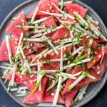 a close of plate of watermelon salad with apple matchsticks, chopped mint, pine nuts and tamari lime dressing.