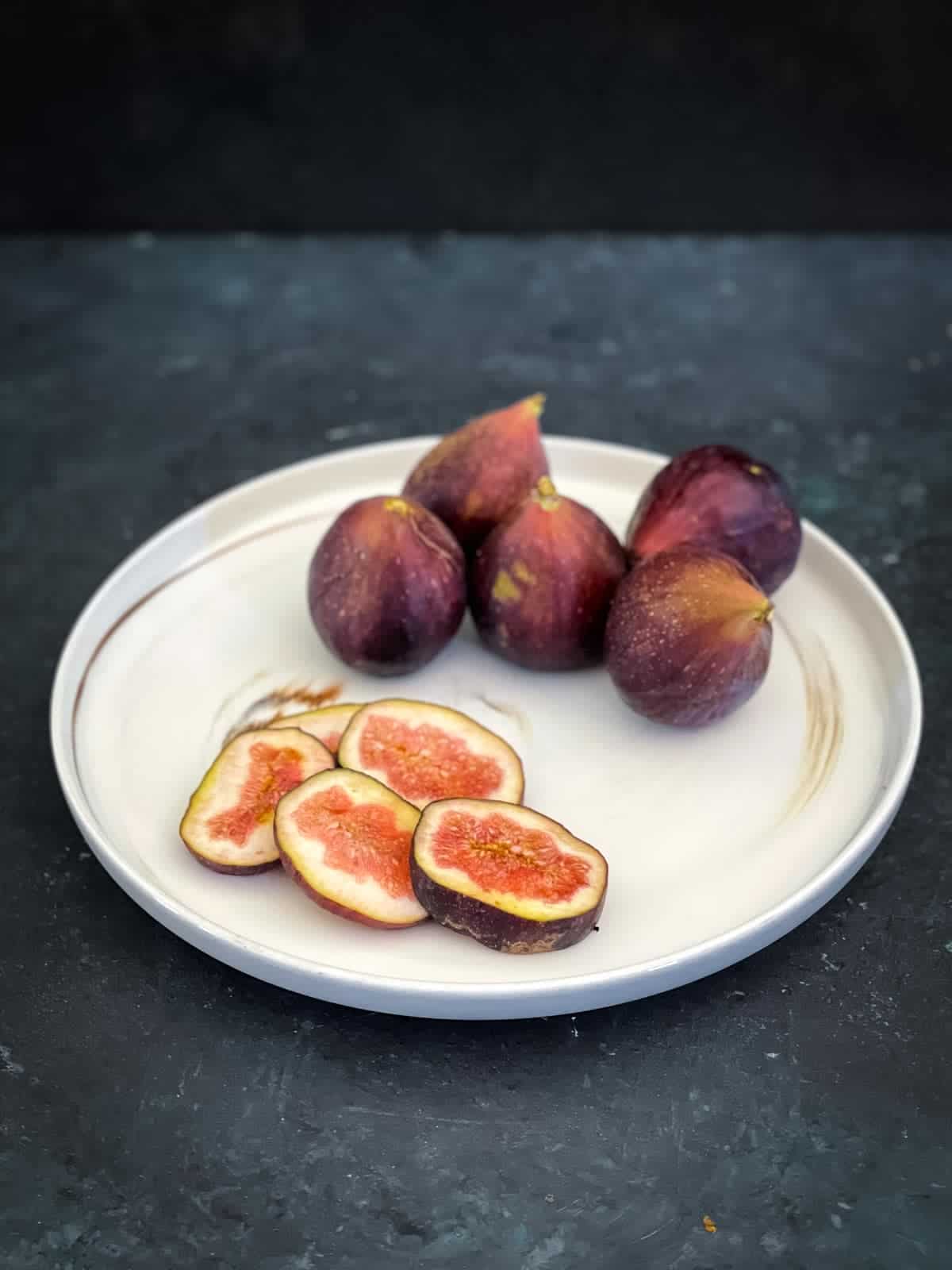Sliced and whole figs on a white marbled plate