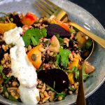 a bowl of freekeh grain salad with roasted beetroot and spiced sumac dressing drizzled on the side. Using gold fork and spoon to serve.
