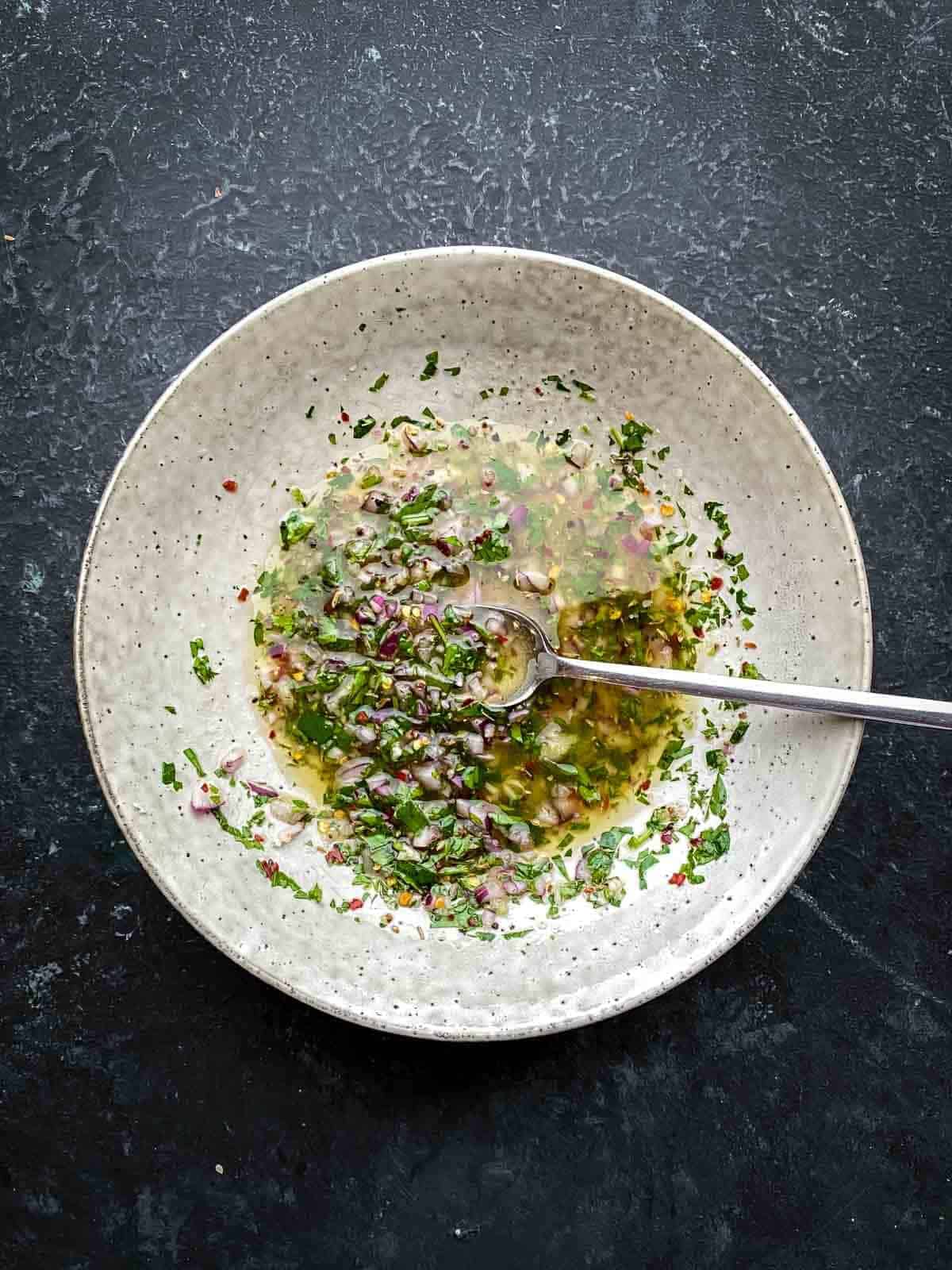 a bowl with parsley vinaigrette with silver spoon in the middle