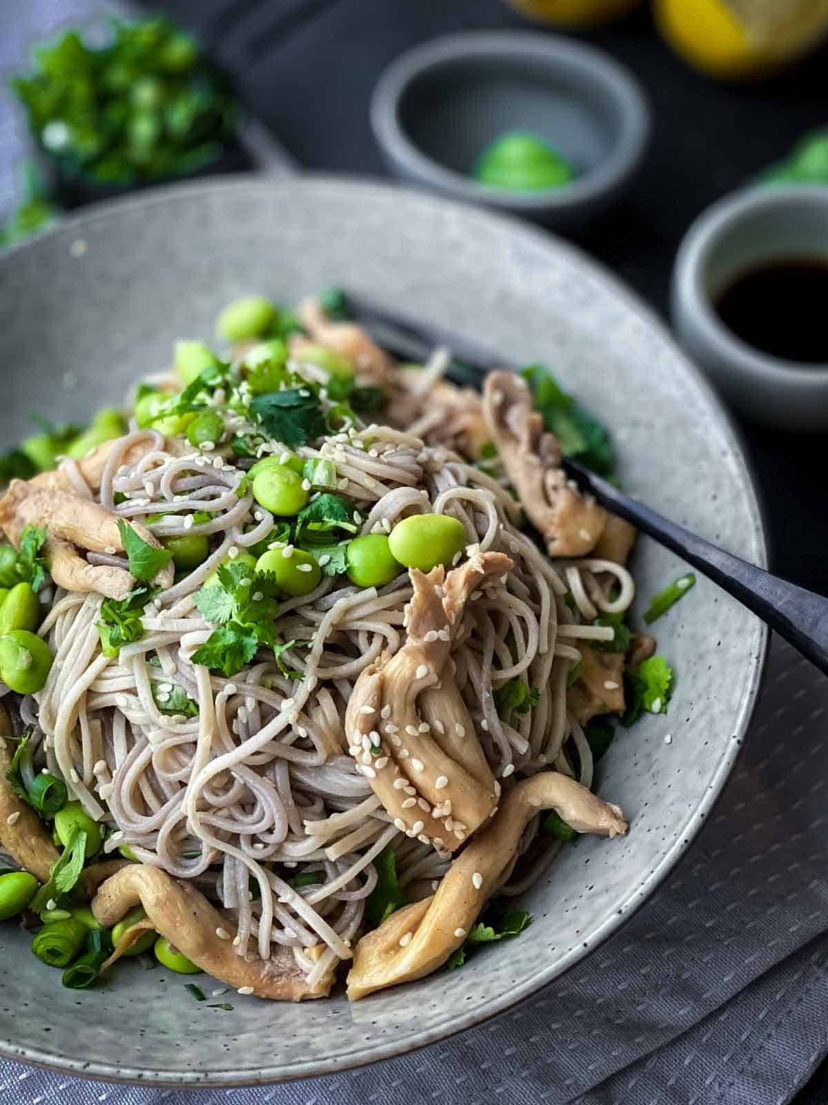 soba noodles, pearl mushrooms, edamame, spring onions, cilantro and sesame seeds served in a grey bowl with fork on side