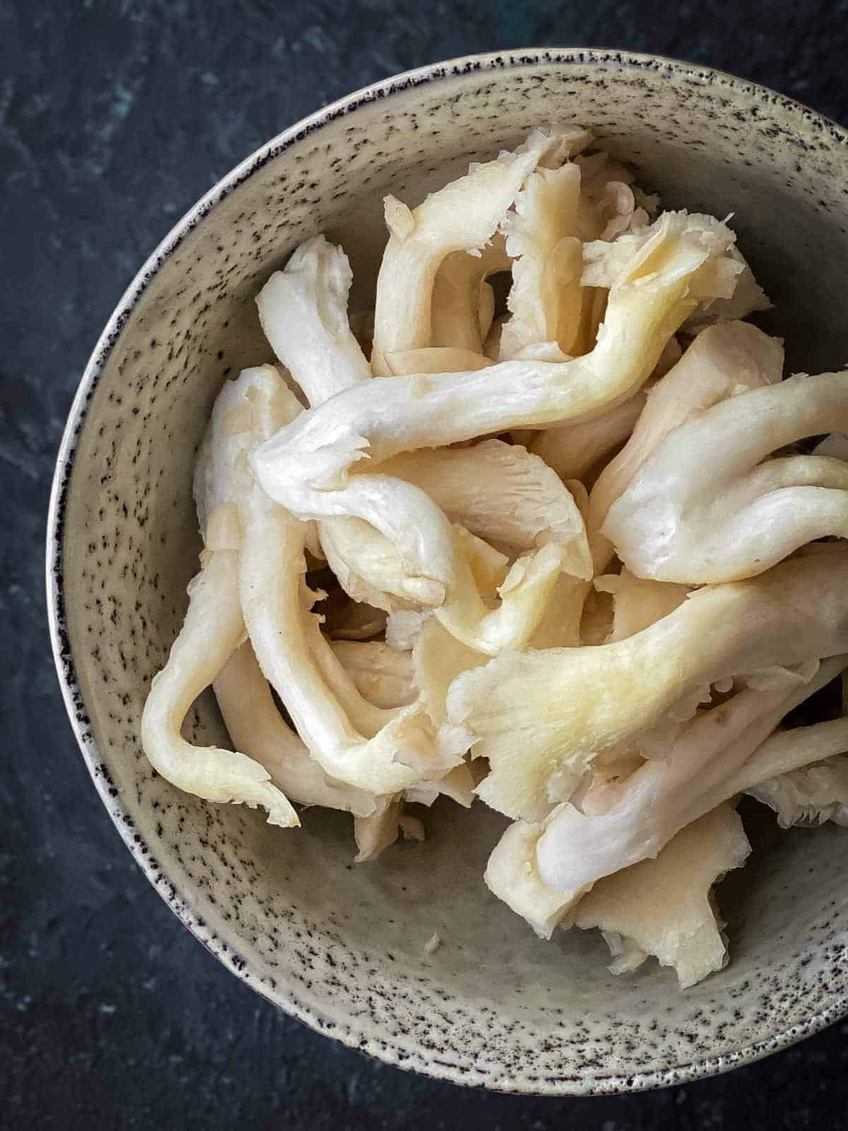 a bowl of raw pearl oyster mushrooms with black background