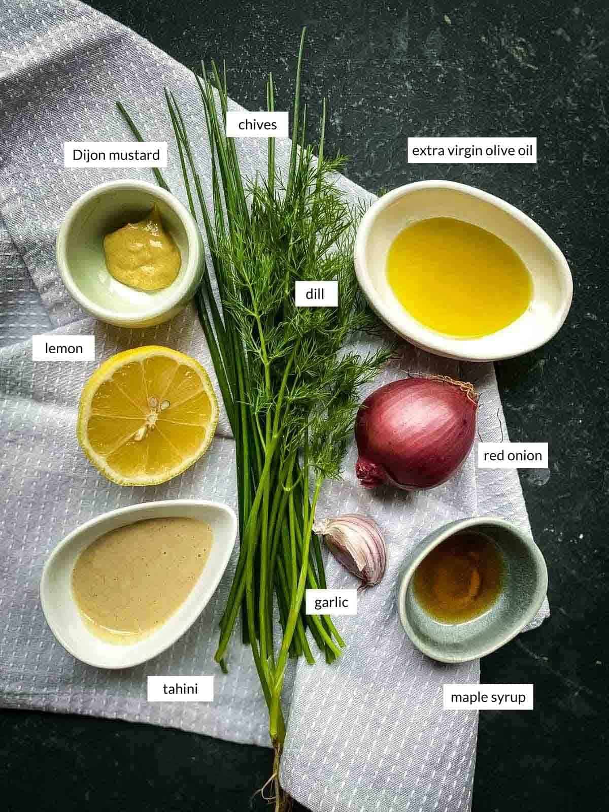 tahini ranch ingredients Dijon mustard, chives, dill, extra virgin olive oil, lemon tahini, garlic, red onion, maple syrup lined up on a grey napkin