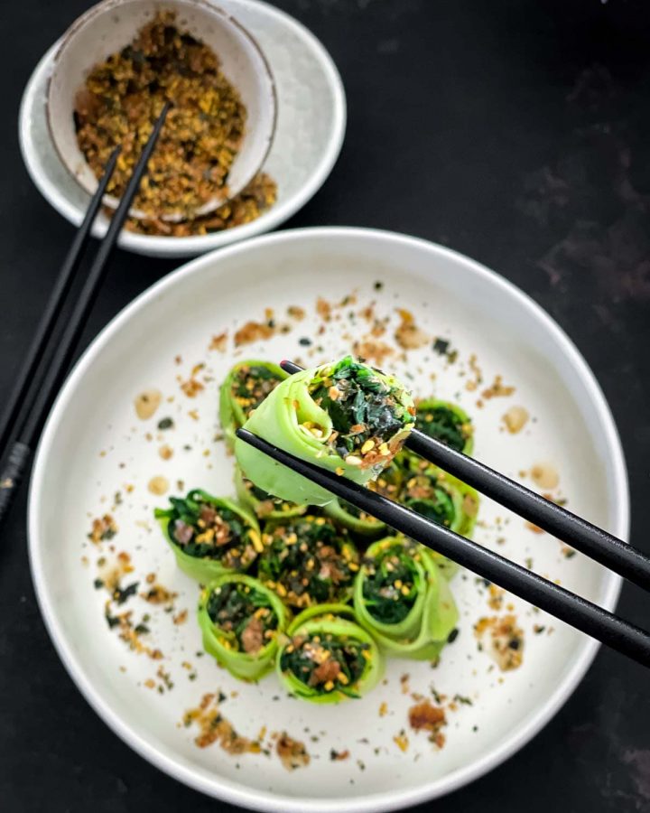 Close up of a Chinese Squash and Spinach Roll held up by a chopstick with furikake in a bowl in the background