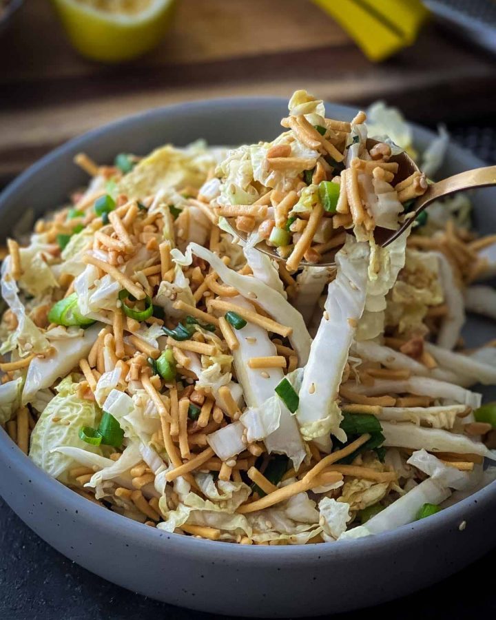 crunchy noodle salad with wombok in a round grey bowl with serving spoon on the right