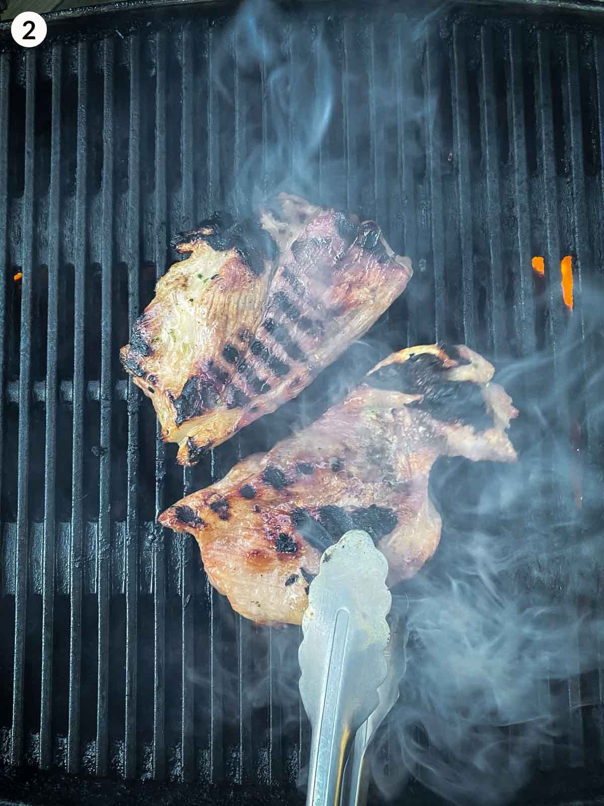 two pieces of pork neck cooking on a grill with steam coming up from the bbq