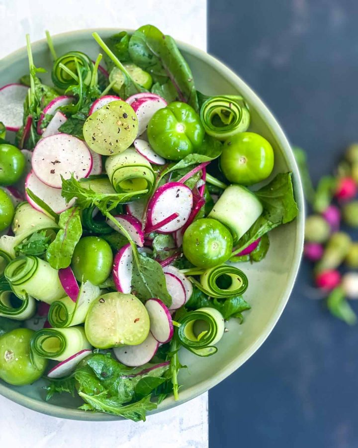 Radish and Tomatillo Salad on a green plate hovering over fresh whole radishes