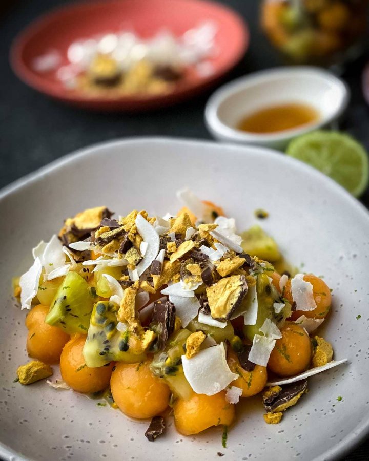 Rockmelon and Passionfruit Salad with Chocolate Honeycomb on a white plate with lime and dressing on the side