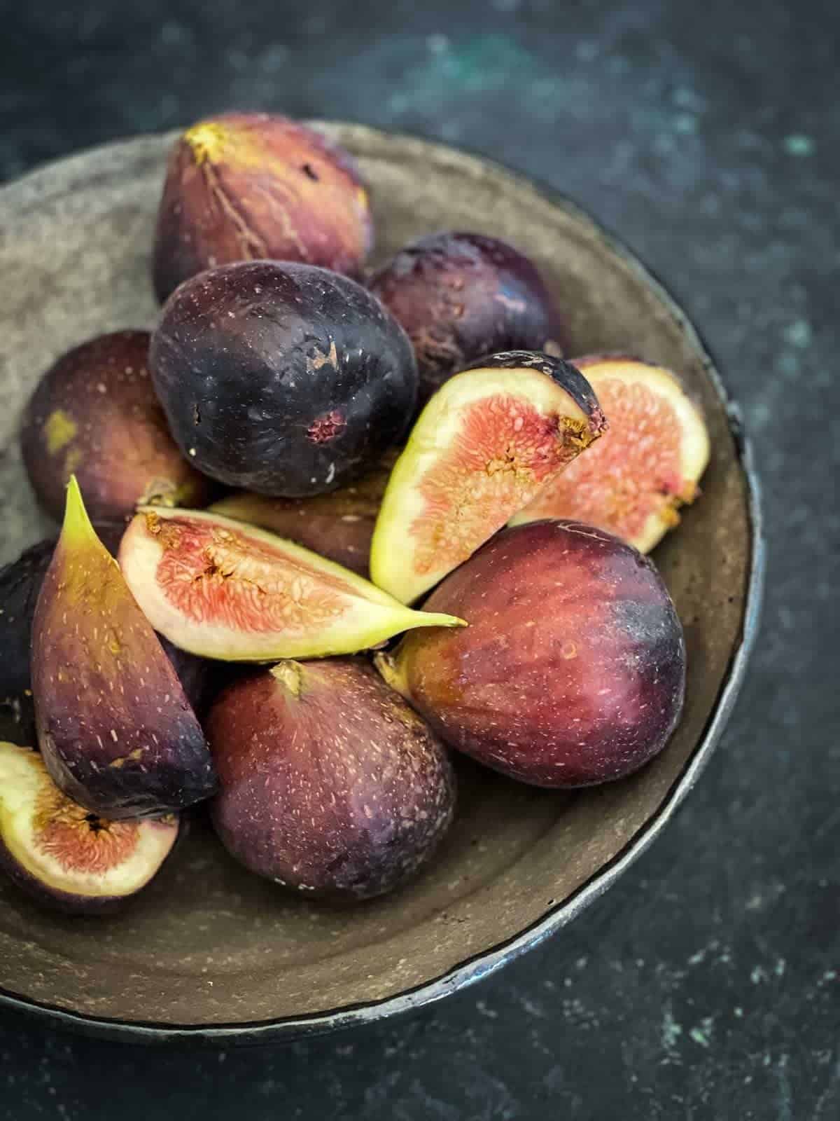 whole and quartered figs heaped on a brown bowl