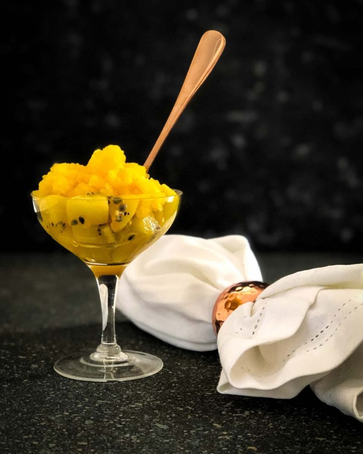 Passionfruit and Kiwi Salad with Tangelo Granita served in a Champagne glass with a gold spoon next to white napkin