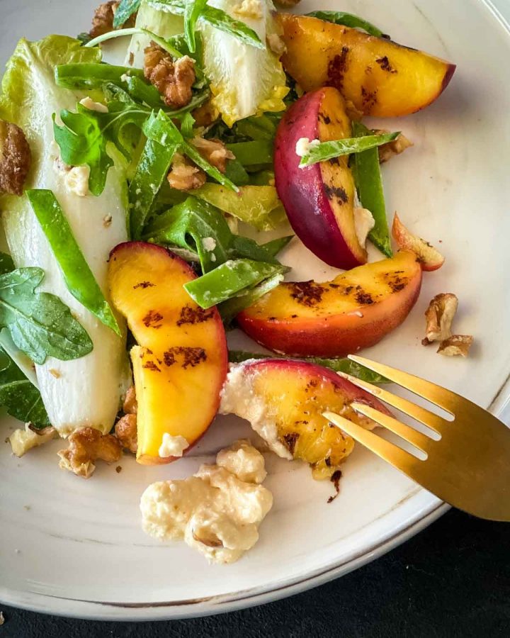 Grilled Peach Salad with Feta on a marble plate with a gold fork