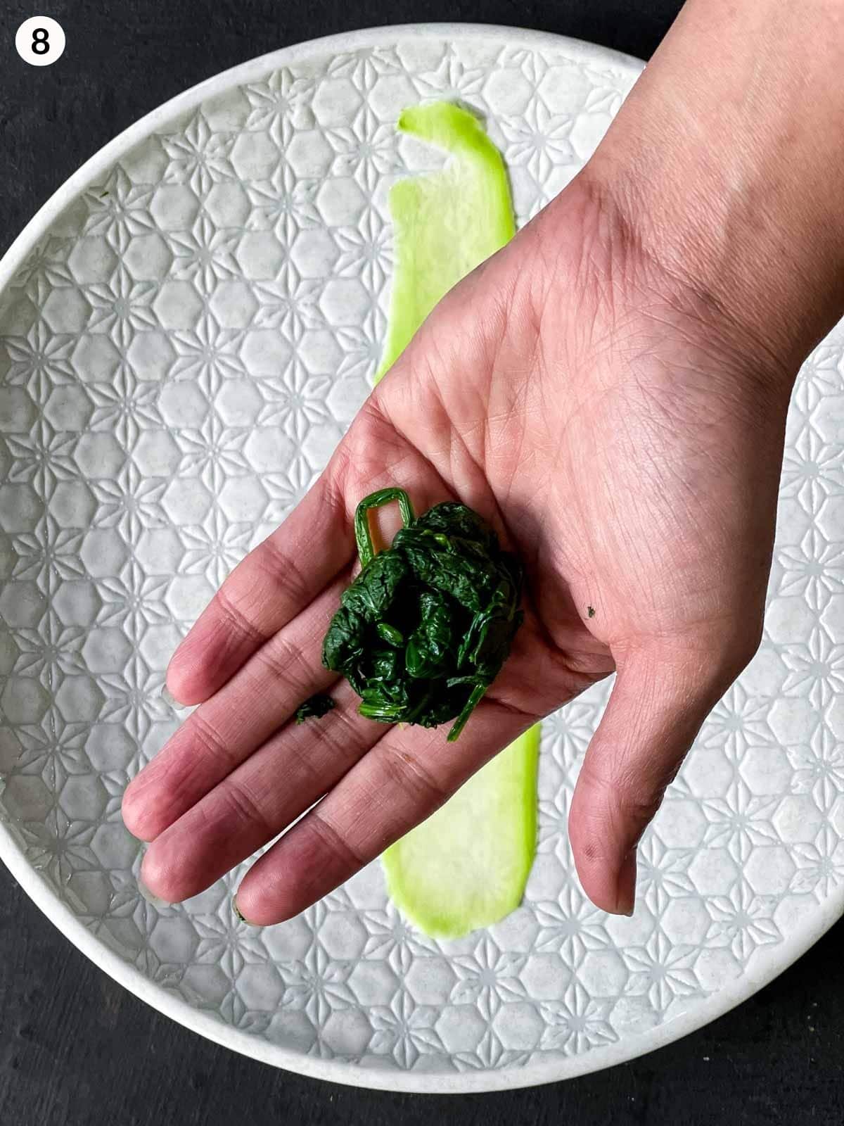 a small amount of cooked spinach in the palm of a hand over a white plate