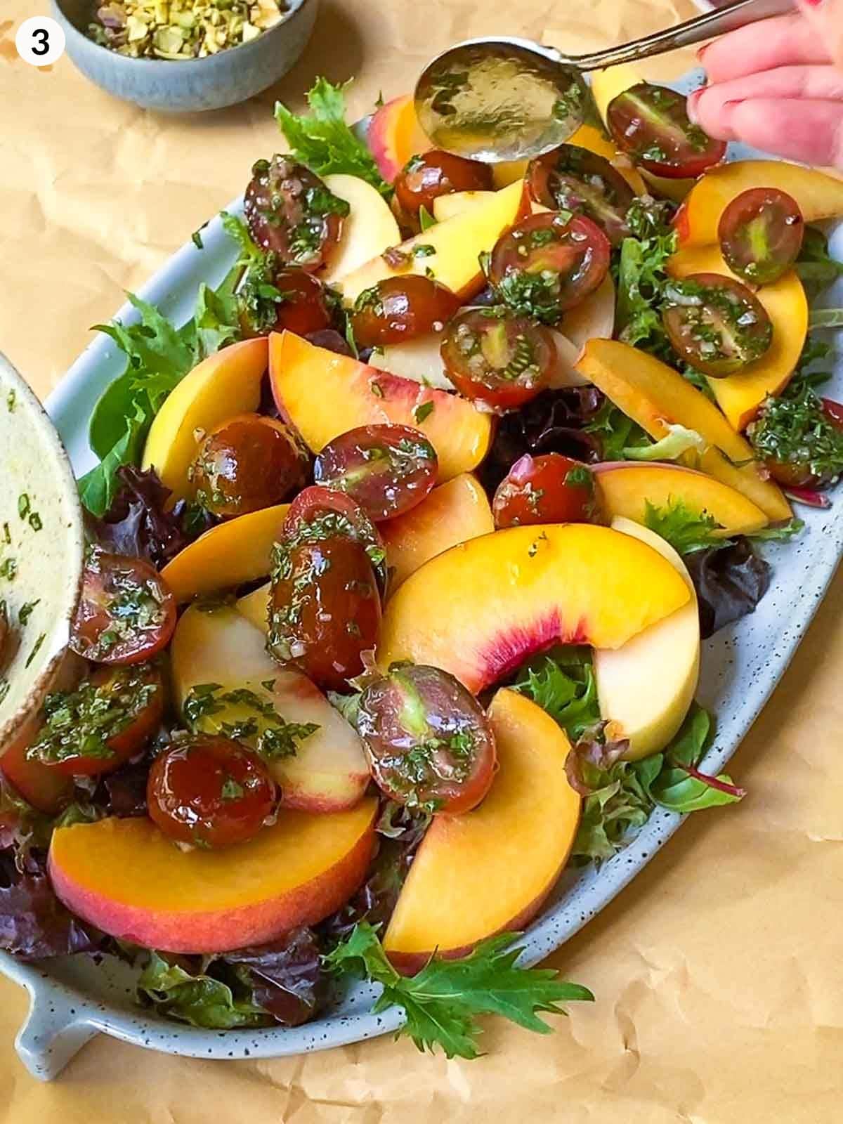 adding cherry tomatoes with basil vinaigrette on top of peaches on platter