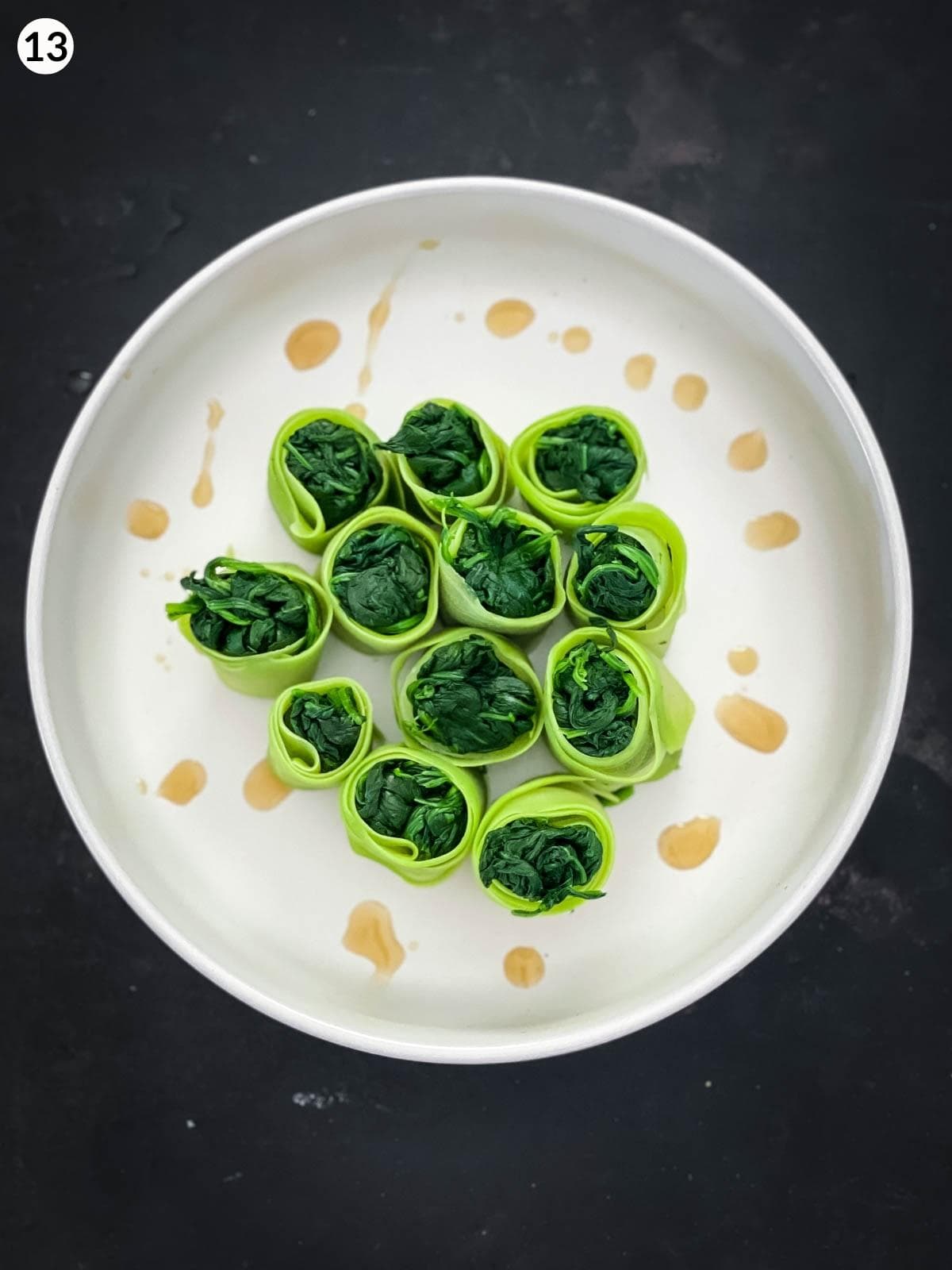 Drops of sesame oil around Chinese Squash and Spinach Rolls in a white serving bowl
