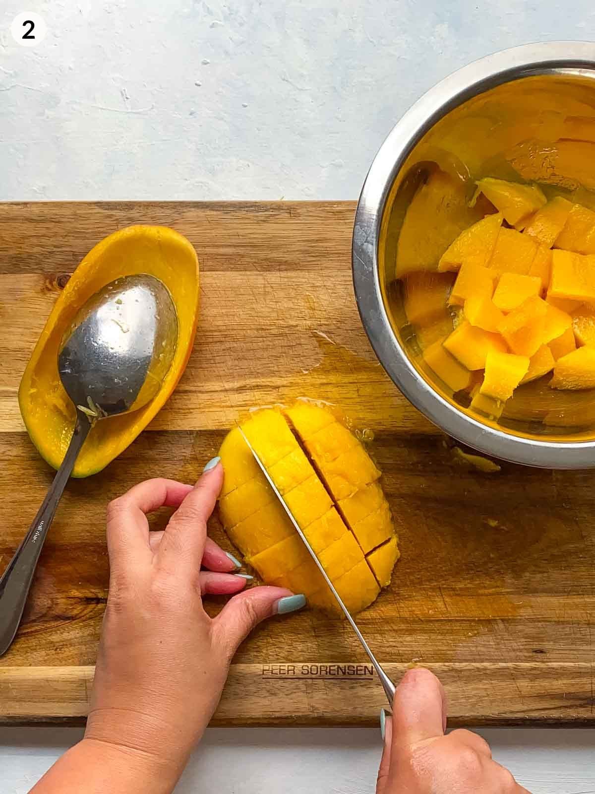 Cutting mango with a knife on a wooden chopping board with a bowl of mango on the side