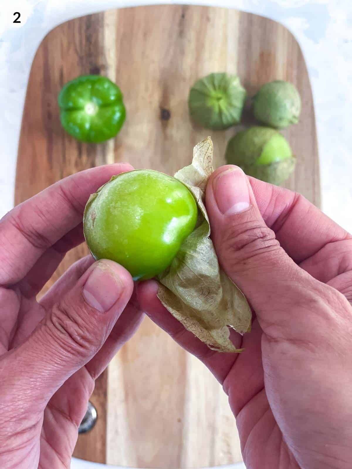 2 hands removing papery husk off a tomatillo