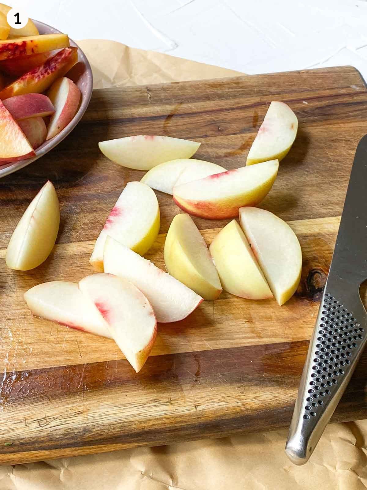cut wedges of peach next a knife on a wooden chopping board