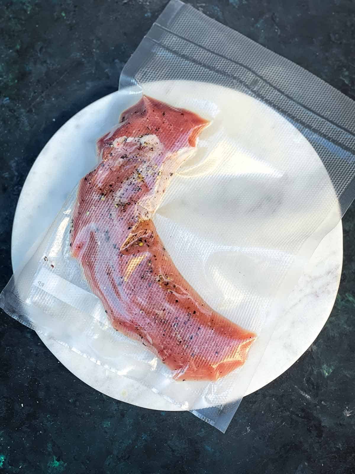preparing sous vide pork tenderloin in a vacuum bag on a white plate