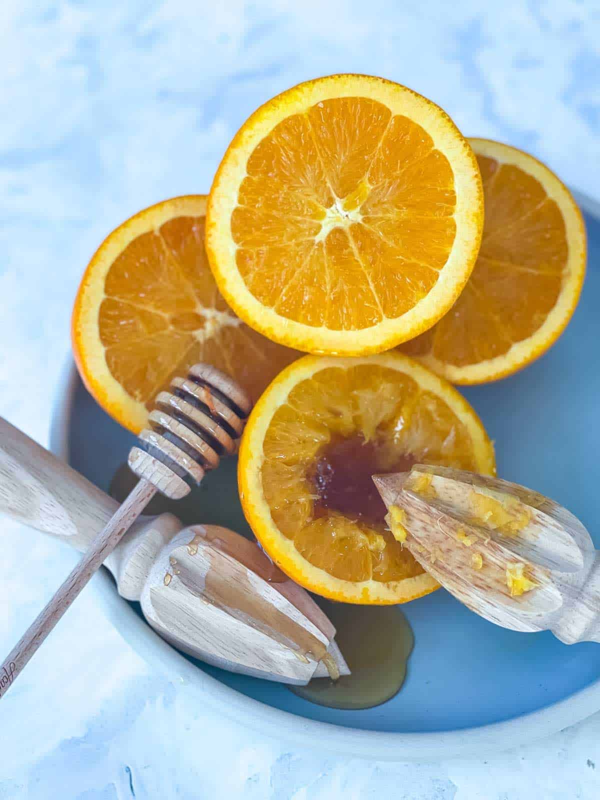 a blue plate of halved oranges being juiced next to a honey twirler