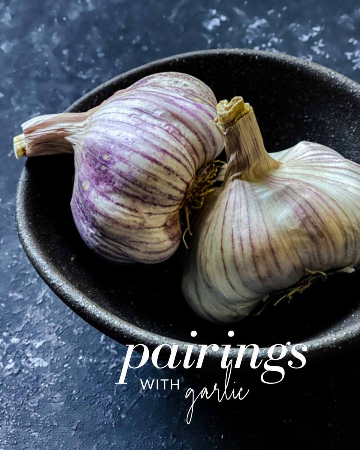 Image of 2 whole garlic bulb in a small black bowl with the text overlay "pairings with garlic"