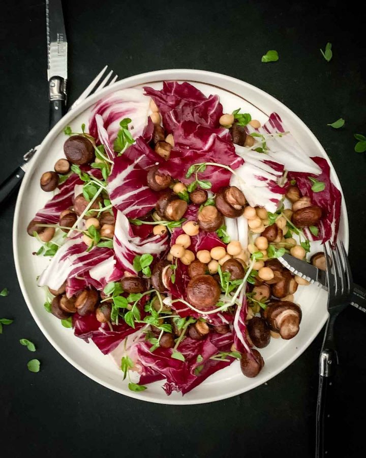 Swiss Brown Mushroom Salad with Chickpeas on a white plate with 2 sets of knives and forks