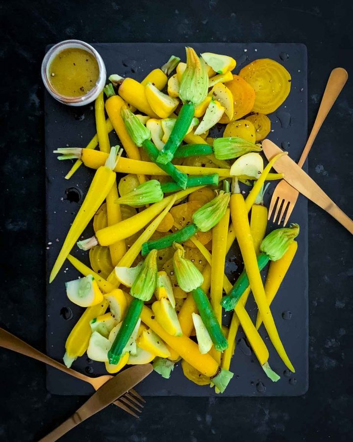 Yellow Salad with Zucchini Flowers on a black slate board with 2 sets of gold cutlery