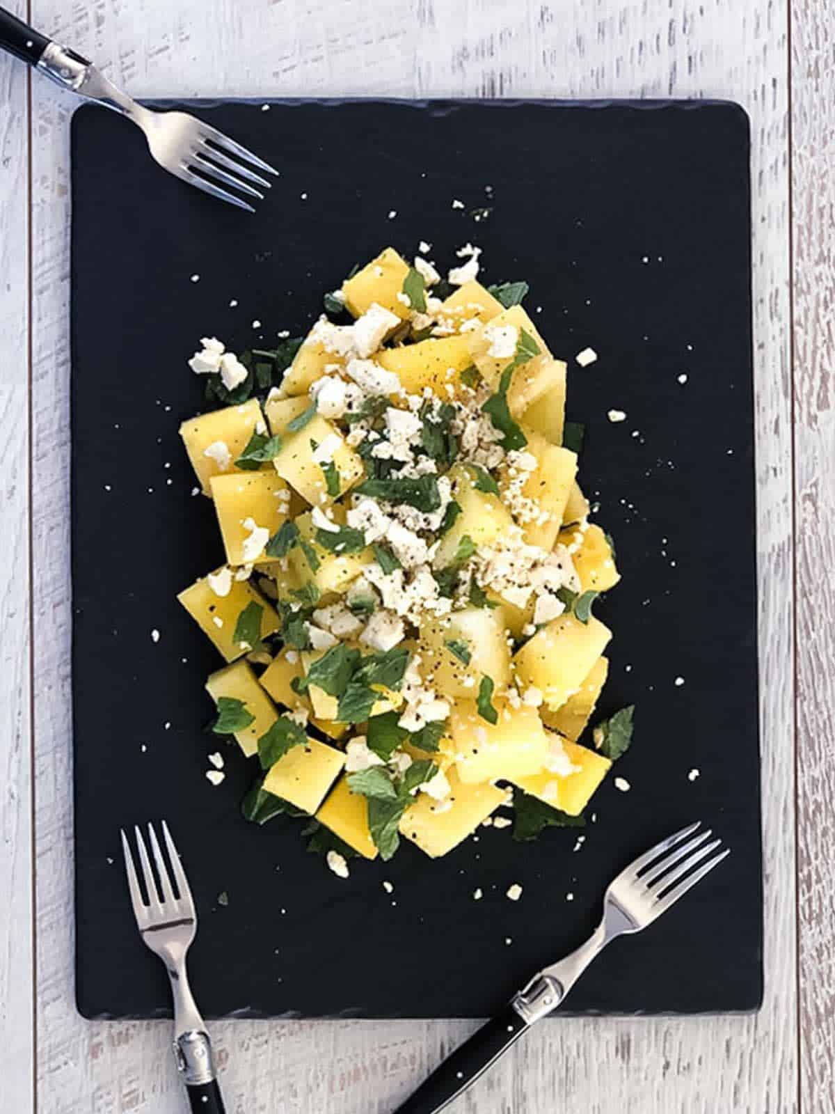 Yellow Watermelon Feta Salad with Mint on a black slate with 2 forks