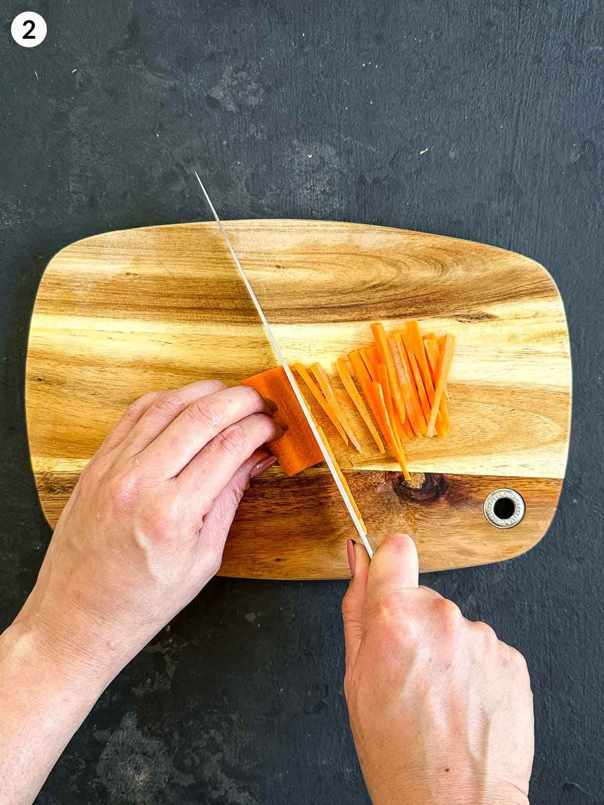 Slicing julienned carrot with a knife on a wooden board