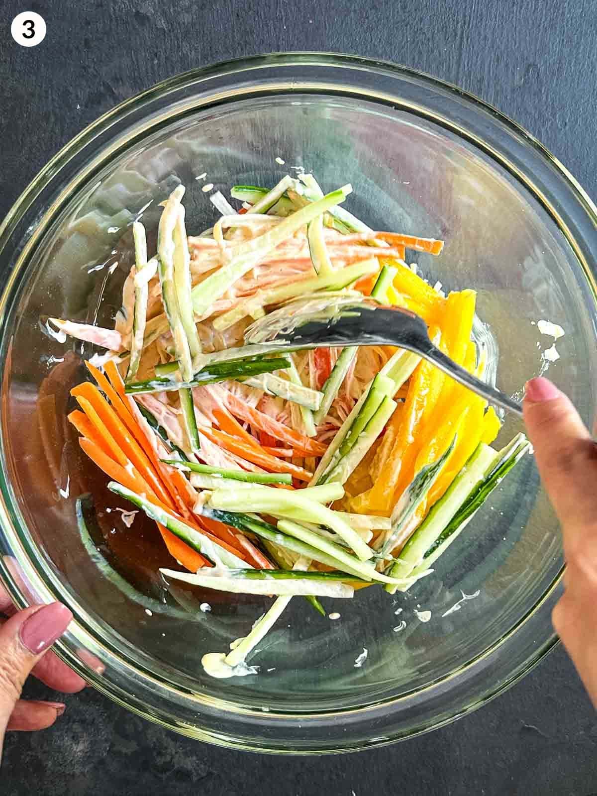 Mixing Kani salad ingredients in a glass mixing bowl with a spoon.