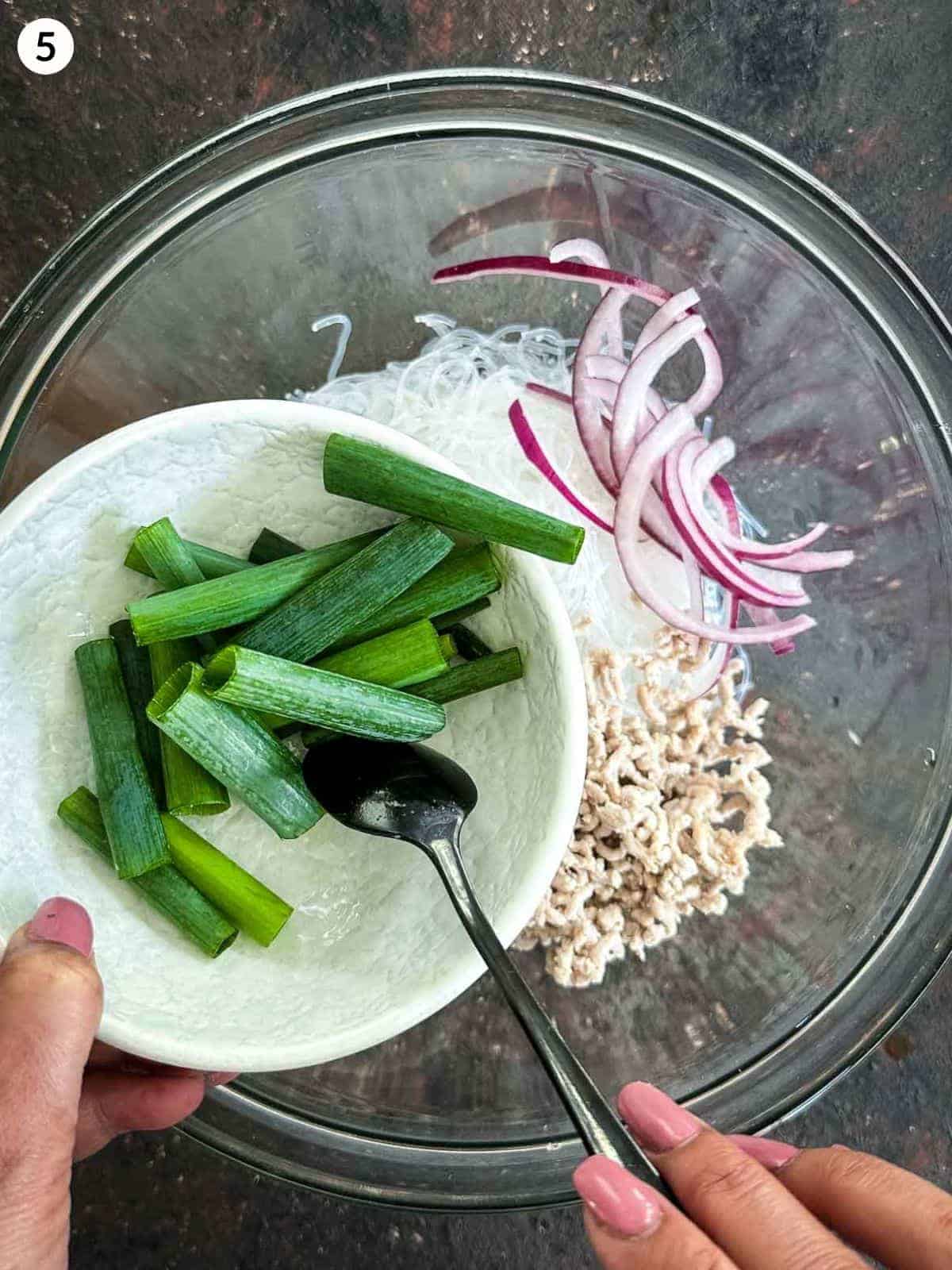 Adding scallions into a glass bowl of yum woon sen ingredients