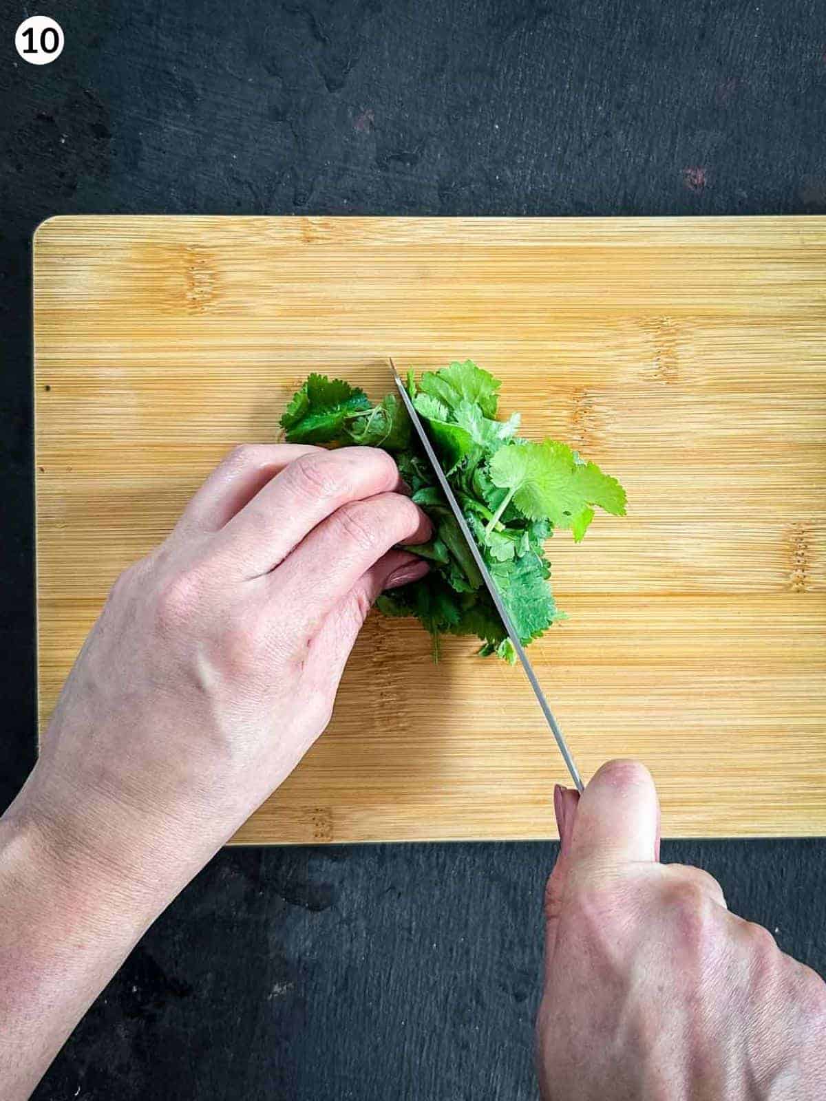 Chopping cilantro with a knife on a wooden board