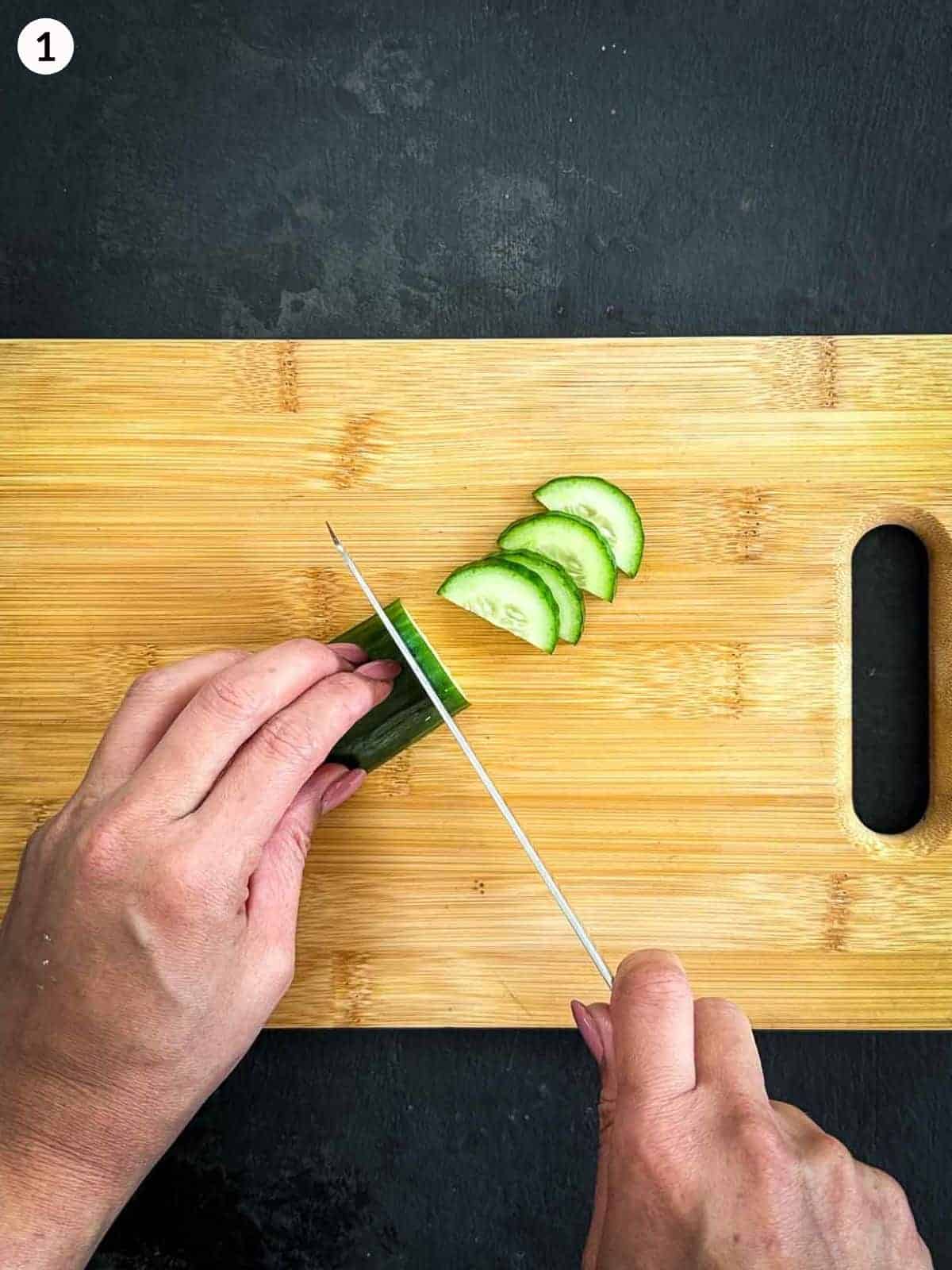Slicing cucumber with a knife on a wooden chopping board