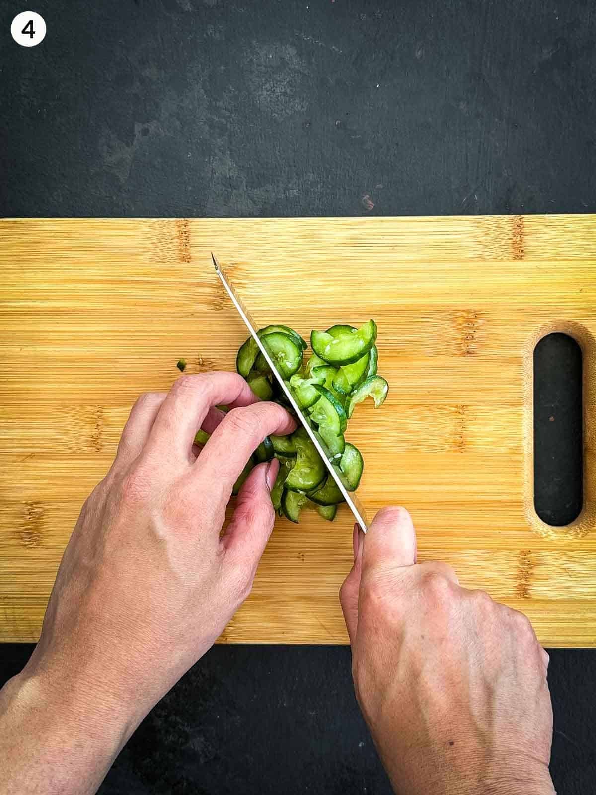 Chopping sliced cucumbers with a knife on a wooden chopping board