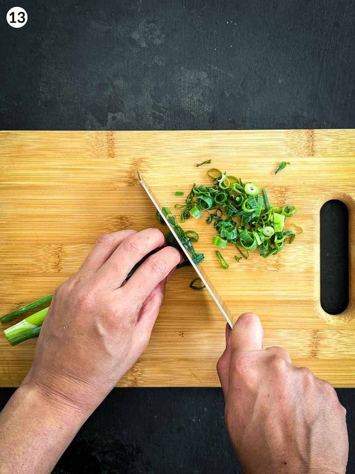 Chopping scallions with a knife on a wooden chopping board