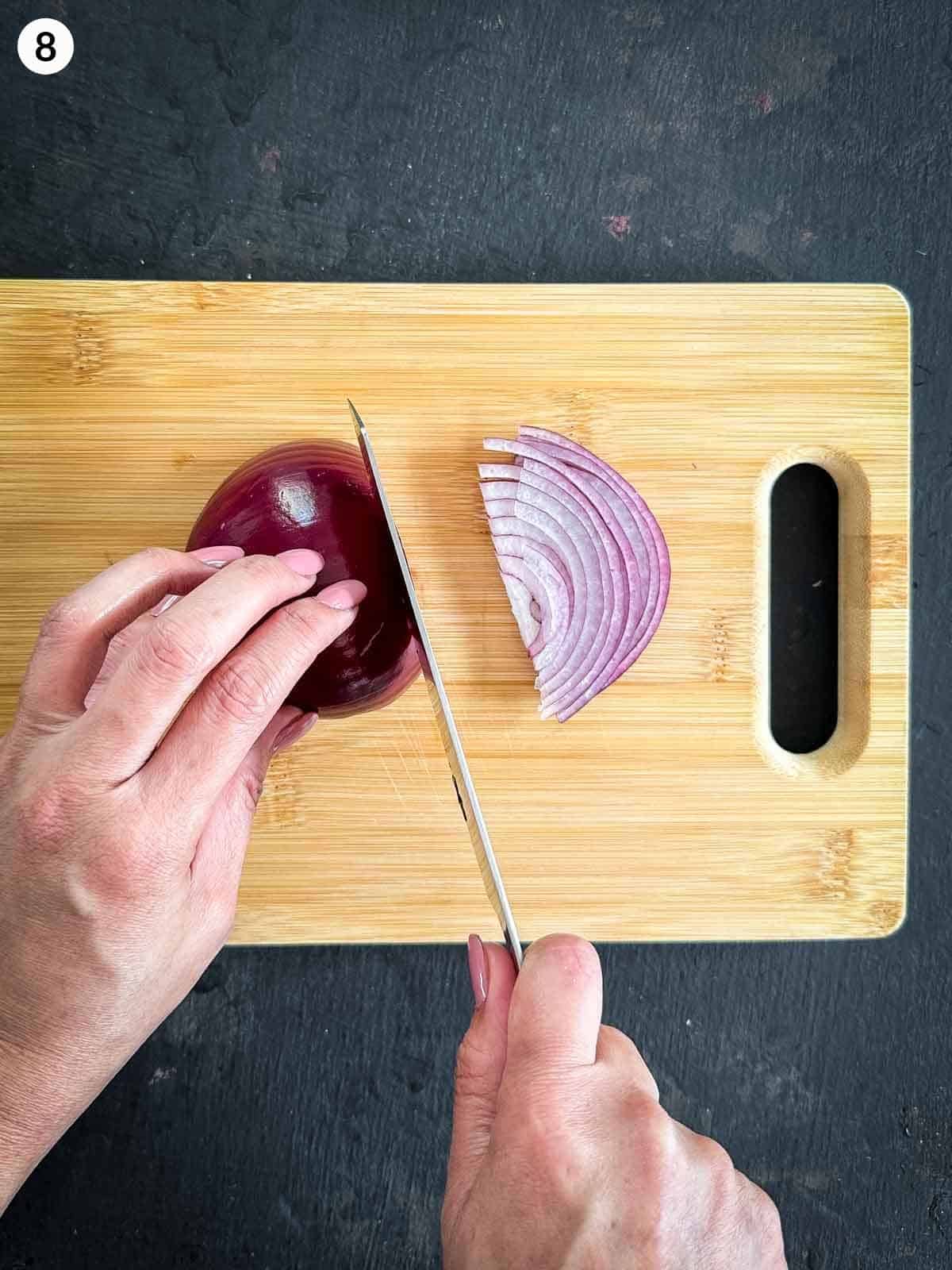 Slicing red onion with a knife on a wooden board