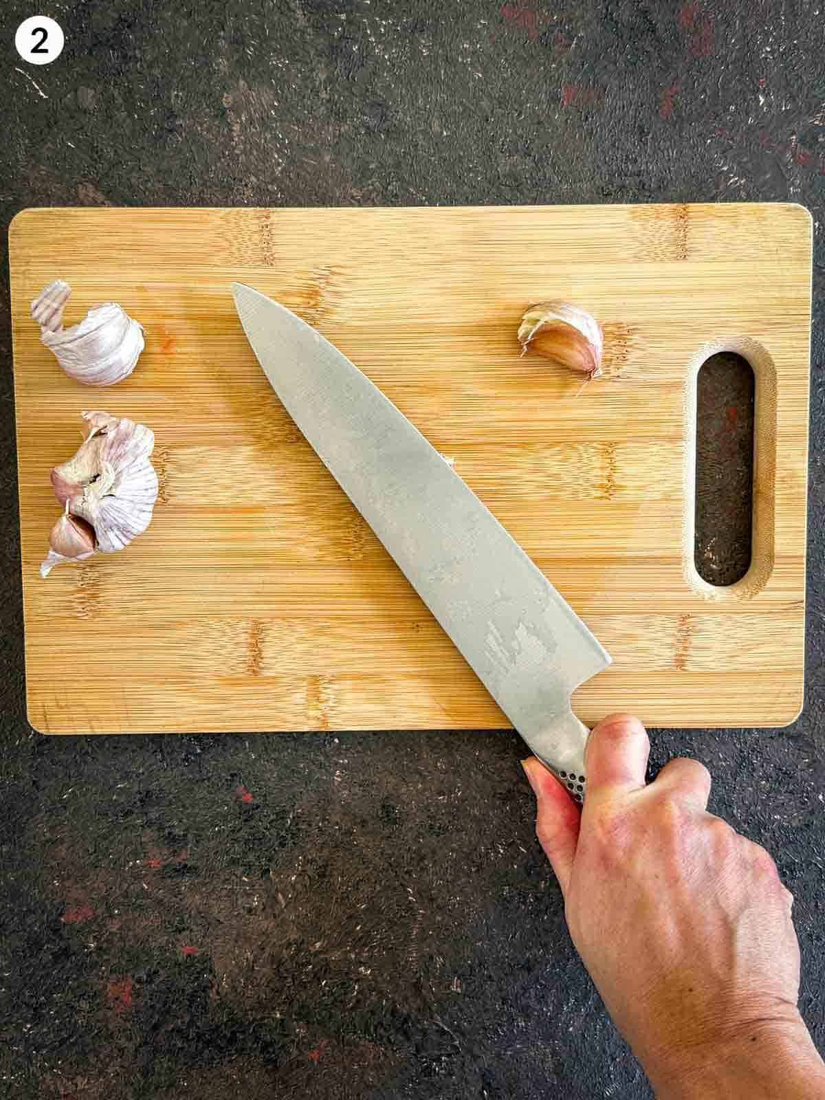 Crushing garlic cloves with a knife on a wooden chopping board