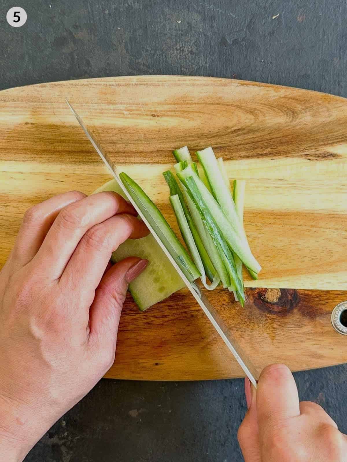 Chopping cucumber with a knife on a wooden board